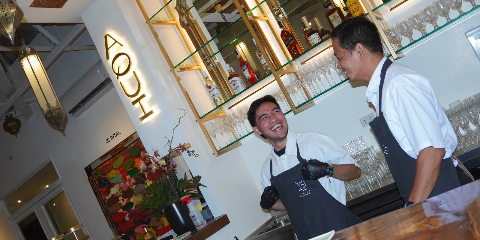 The Aqui bar: one of the team laughing under the lit AQUI sign and the arched mirrors