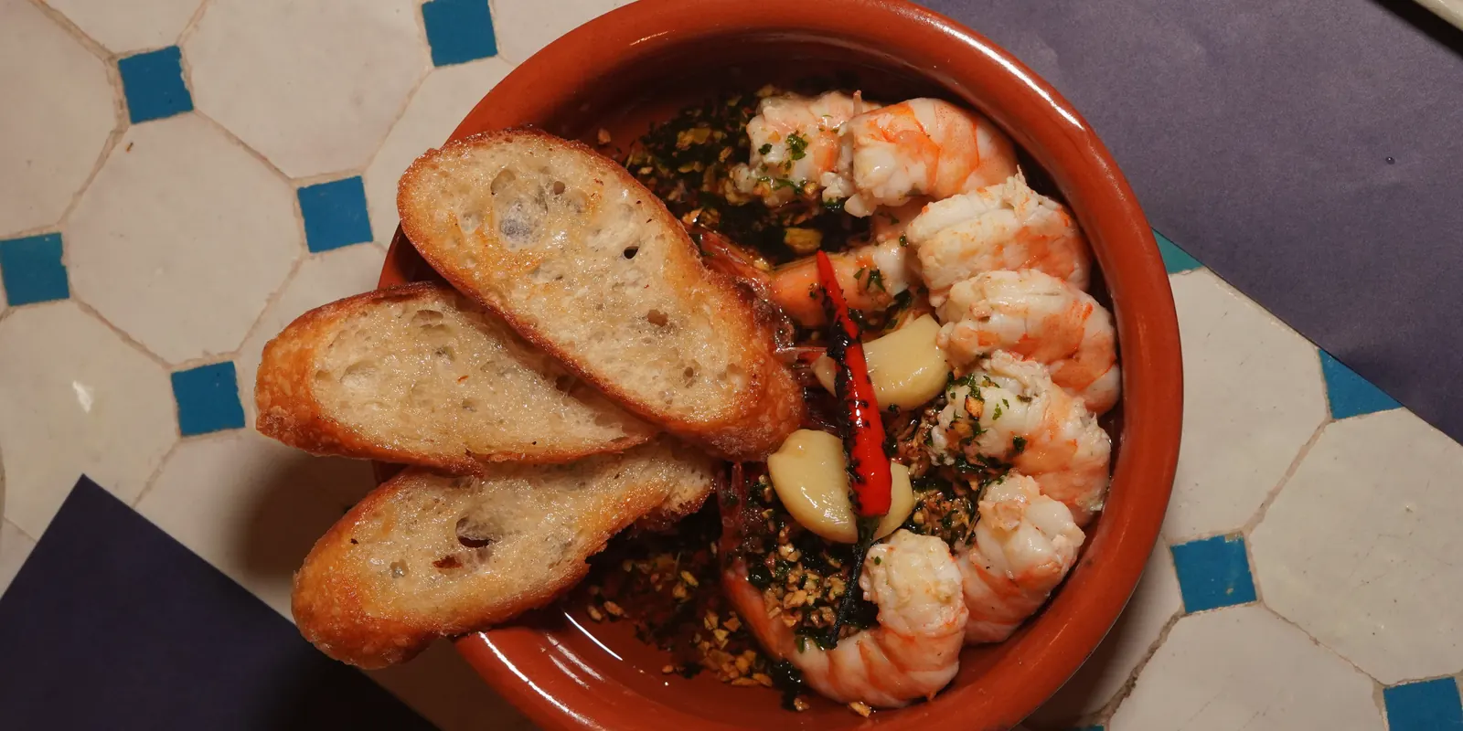 Gambas al ajillo with toasted baguette on a blue-and-white tiled table