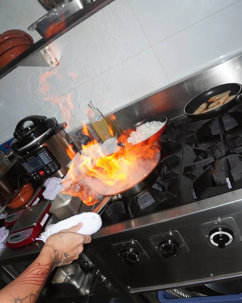 A pan flares on the range in Aqui’s kitchen