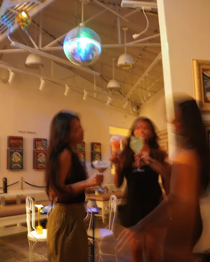 The gallery after dark: guests with drinks moving under the disco ball, paintings on the walls