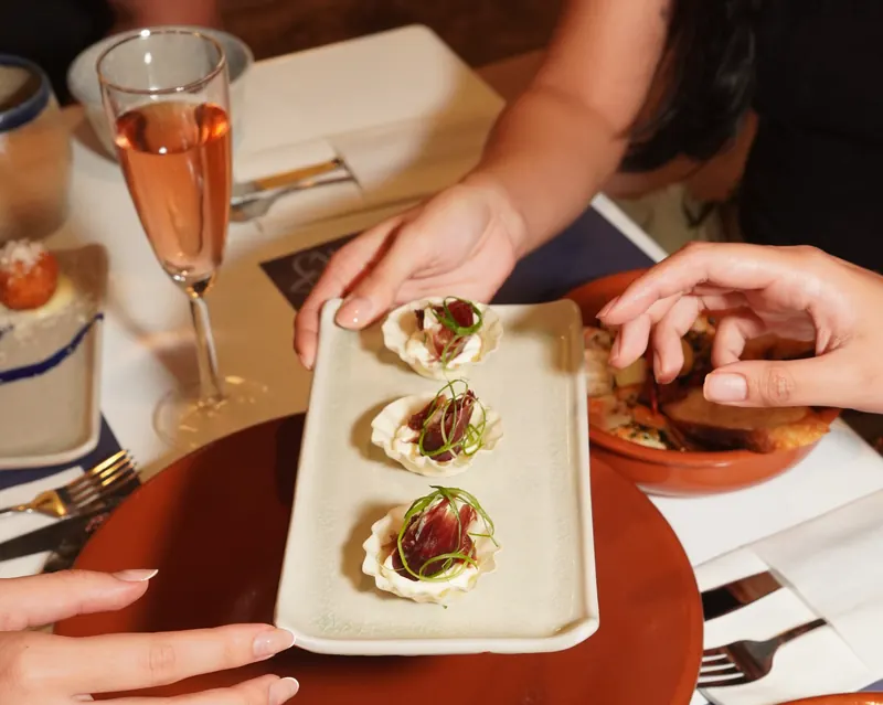 A plate of pintxos passed across the table, a glass of rosé beside it